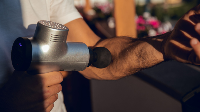 A person using a massage gun to massage their arm.